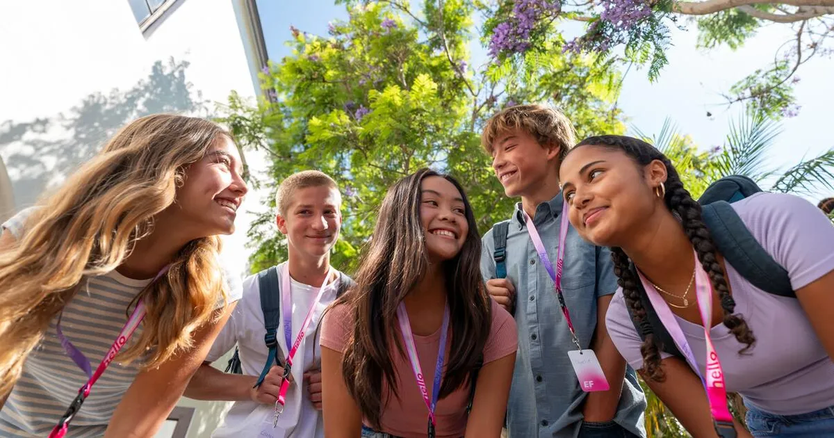 Grupo de estudiantes de EF con credenciales «hello», sonriendo al aire libre